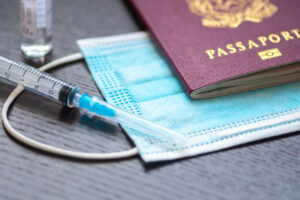 Syringe with needle, vial, surgical face mask and passport or visa on a white table ready to be used. Covid or Coronavirus vaccine background