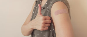woman showing thumb up and her arm with bandage after got vaccinated or  inoculation