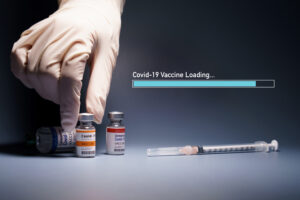 Covid-19 Vaccine Research and Development progress – Global trial phase 3 concept. Hand of a researcher take a 2019-nCov vaccine vial with loading bar and syringe needle beside. Hope, Support, Success