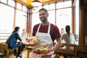 Portrait of male deli owner holding food in restaurant